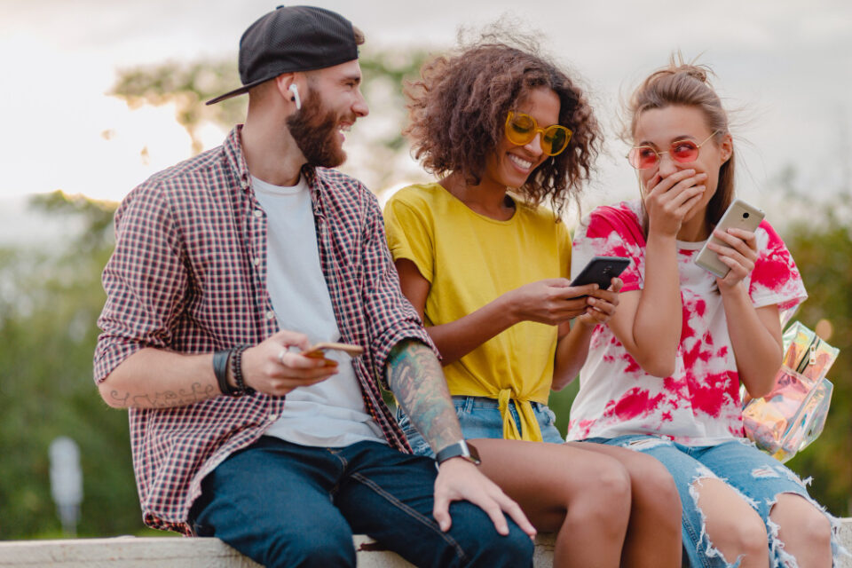 happy-young-company-smiling-friends-sitting-park-using-smartphones-man-women-having-fun